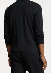 Svart långärmad topp med rund halsringning, tillverkad av mjukt tyg. Har åtsittande manschetter och en avslappnad design i ryggen. Kombineras med matchande byxor.