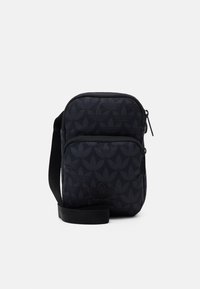 Sacoche noire compacte d'Adidas avec un motif trefoil subtil, poche zippée à l'avant et bandoulière réglable.