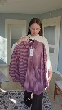 Camicia a maniche lunghe, con bottoni, color marrone rossiccio con strisce bianche verticali. Presenta un colletto a punta e una targhetta appesa. Tessuto in cotone, vestibilità comoda.