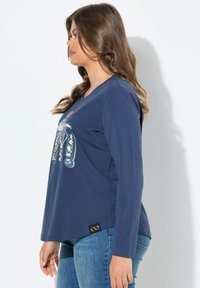 Námořnická košile s dlouhým rukávem, která obsahuje grafický design na přední straně, zakulacený lem a malou nášivku loga na dolní levé straně.