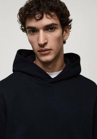 Hoodie nero con una vestibilità comoda e un cappuccio regolabile, realizzato in tessuto morbido. Presenta un design semplice e uno stile minimalista.