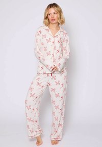 Wit pyjama set met een rood strik en kersenpatroon. Zachte stof met lange mouwen, een knoopsluiting aan de voorkant en losse broekspijpen.