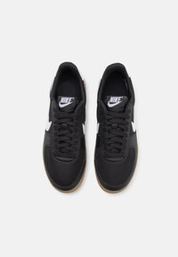 Paire de baskets noires Nike avec logos swoosh blancs, lacets noirs et semelles marron, vues de dessus sur un fond uni.