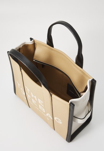 Tan and black leather tote bag with top handles, structured design, contrasting colors, and an interior zippered pocket. Features brand logo.