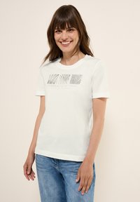T-shirt en coton blanc à manches courtes et col rond. Présente un design graphique gris sur le devant avec le texte "élargir les horizons."