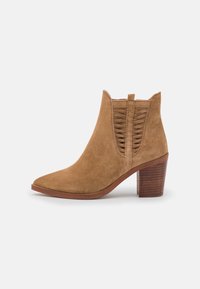 Tan-nahka nilkkuri, jossa on pinottu puinen lohkare, ja kudottu elastinen sivupaneeli valkoista taustaa vasten.