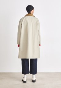 Beige coat with a brown collar, long sleeves, and a loose fit. Paired with dark denim cropped pants and white socks.