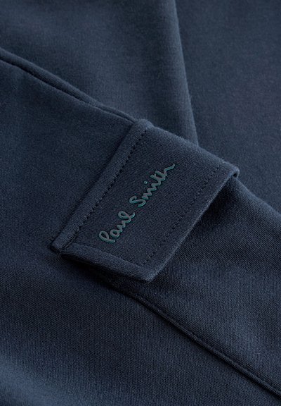 N�ámornícka modrá bavlnená tkanina s hladkou textúrou, na strane je prišitý obdĺžnikový štítok s nápisom "Paul Smith" v tyrkysovom písmovom štýle.