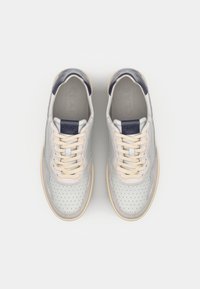 Sneakers gri deschis cu un design perforat, șireturi crem și accente bleumarin pe călcâi și limbă. Talpă din cauciuc. Paletă de culori neutră.