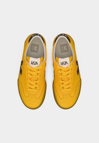 Κίτρινα αθλητικά παπούτσια με λείο δερμάτινο επάνω μέρος, στρογγυλή μύτη και αντιθετικές σκουρόχρωμες λεπτομέρειες. Διαθέτουν επίπεδα κορδόνια και μαξιλαρωμένο εσωτερικό.