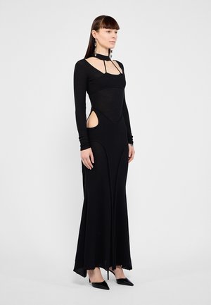 Abito nero a maniche lunghe con fessure laterali, texture a coste e collo alto. Presenta un busto aderente e una gonna fluida. Scarpe con punta affilata.