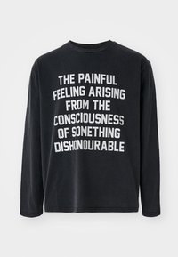 Cămașă neagră cu mânecă lungă din bumbac, cu text alb îndrăzneț și un citat centrat pe față. Guler rotund și croială confortabilă.