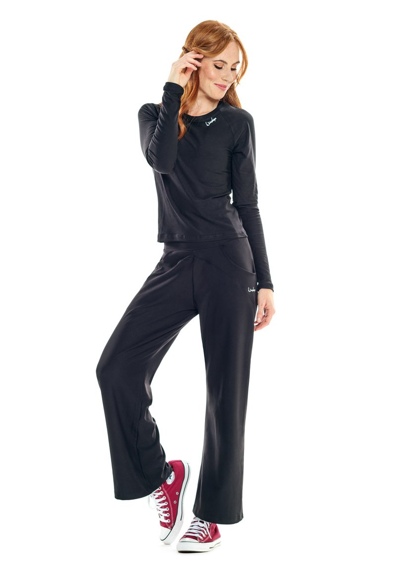 Black long-sleeve top with a round neckline, paired with black loose-fit pants featuring front pockets, worn with red and white sneakers.