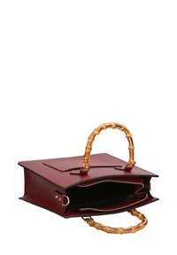 Bordeaux leren handtas met bamboe handvat, ritsluiting en een zak aan de voorkant. Interieur is zwart met twee compartimenten.