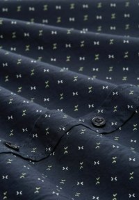Navy shirt fabric with a textured finish, featuring a pattern of small white and green geometric shapes, and a black button detail.