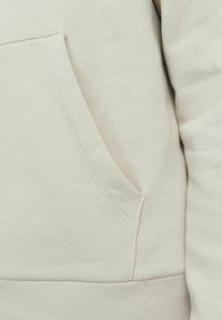 Light beige hoodie featuring a kangaroo pocket, ribbed cuffs, and a soft texture, with visible stitching detail on the pocket.