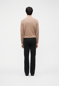 Πλεκτό μπεζ πουλόβερ με μακριά μανίκια, συνδυασμένο με μαύρο παντελόνι. Το ύφασμα φαίνεται λείο με ελαφριά γυαλάδα και εφαρμοστή σιλουέτα.