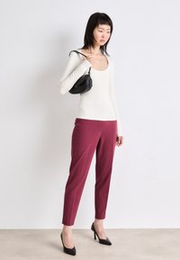 Witte, langmouwige top, aansluitend; bordeauxrode, op maat gemaakte broek; zwarte handtas met gebogen ontwerp; zwarte hoge hakken. Minimalistische stijl, neutraal palet.