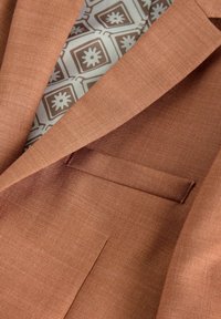 Blazer de color óxido con una tela texturada, que presenta un bolsillo sutil y un forro interior con un patrón en tonos claros.