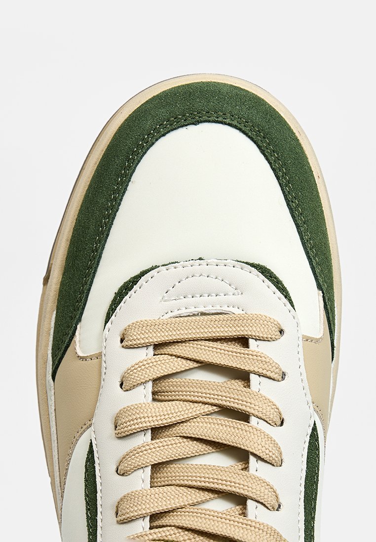 Sneaker con una base in pelle bianca, accenti in suede verde, lacci beige e una suola texturizzata, che mette in mostra un design classico e un contrasto di colori.