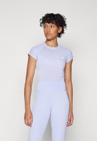 Svetlofialové športové crop top s krátkymi rukávmi a hladkou textúrou. Kombinované s ladiacimi legínami s vysokým pásom, oboje s minimálnym dizajnom.