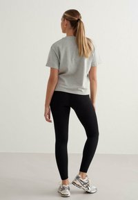 Graues Baumwoll-T-Shirt mit kurzen Ärmeln, kombiniert mit schwarzen gerippten Leggings und silbernen Sportschuhen, von hinten betrachtet.