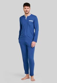 Top azul de manga larga con un cuello y un bolsillo azul claro, combinado con pantalones azules a juego. Tejido suave y liso con un diseño ajustado.