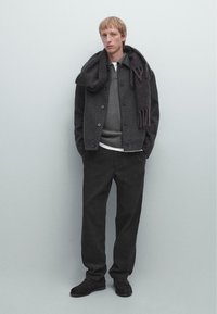 Dark grey wool coat, grey sweater, white shirt, black pants, and black shoes. A dark scarf with fringe drapes casually over the coat.