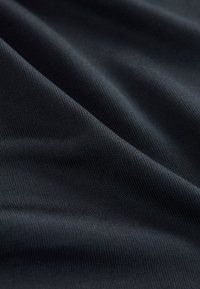 Schwarzer Stoff mit einer strukturierten, gerippten Oberfläche, die Falten und Knicke zeigt und dadurch seinen dreidimensionalen Charakter betont.