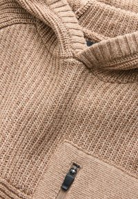 Beige Strick-Hoodie mit strukturiertem Muster, ausgestattet mit einem halbseitigen Reißverschluss und einer vorderen Tasche mit einem Metallreißverschluss.