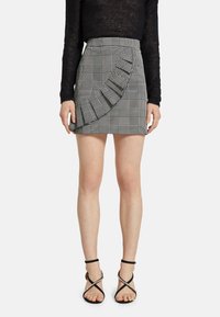 Černobílá kostkovaná sukně s volánkovými detaily na jedné straně, se zvýšeným pasem a rovný střih. V kombinaci s černými sandály na tenkých páscích.