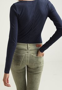 Marinblå långärmad topp med en jämn textur, ihop med ljusgröna kordbyxor med bakfickor och en läderetikett på midjebandet.