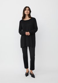 Tunica nera a maniche lunghe realizzata in tessuto morbido, abbinata a pantaloni neri slim-fit e décolleté neri a punta. Design semplice, senza motivi.