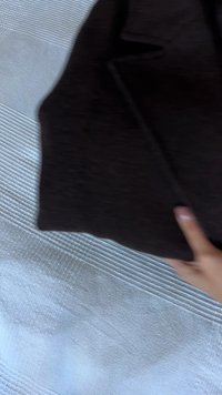 Ţesătură texturată de culoare maro închis, cu o suprafaţă netedă, având o margine pliată şi cusături vizibile. Mână parţial vizibilă ţinând ţesătura.