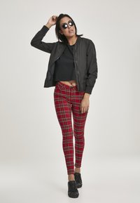 Must kollane bomber-jakk, must lühike T-särk, punase ruuduga retuusid roheline ja kollane joonega, mustad spordijalatsid ja ümmargused prillid. Siledad tekstuurid.