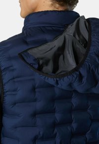 Marineblaues Steppweste mit hohem Kragen und Kapuze. Das Innere der Kapuze hat eine glänzende schwarze Fütterung. Gepolsterte Abschnitte sind deutlich gesteppt.