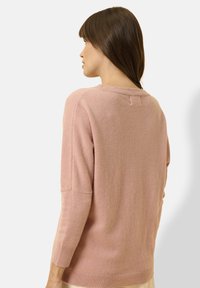 Maglione lungo a maniche, di colore rosa chiaro, realizzato in un morbido materiale lavorato a maglia. Presenta un collo rotondo e cuciture delle spalle scese. Dettaglio di trama delicata.