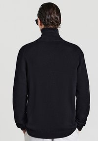 Schwarzer Strickpullover mit hohem Kragen, gerippten Bündchen und Saum. Der Stoff hat eine glatte Textur und ein tailliertes Design.