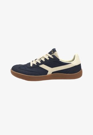 Zapatilla baja azul marino y beige con cordones blancos y suela de goma color caramelo, vista desde el lado exterior.