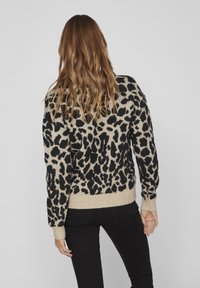 Pull en maille à motif léopard en crème et noir. Comprend des poignets et un ourlet côtelés; texture douce; coupe décontractée.