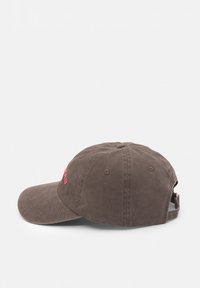 Barna pamut baseball sapka íves karimával, állítható pánttal és piros hímzett szöveggel az elején. Szellőzőlyukakkal rendelkezik.