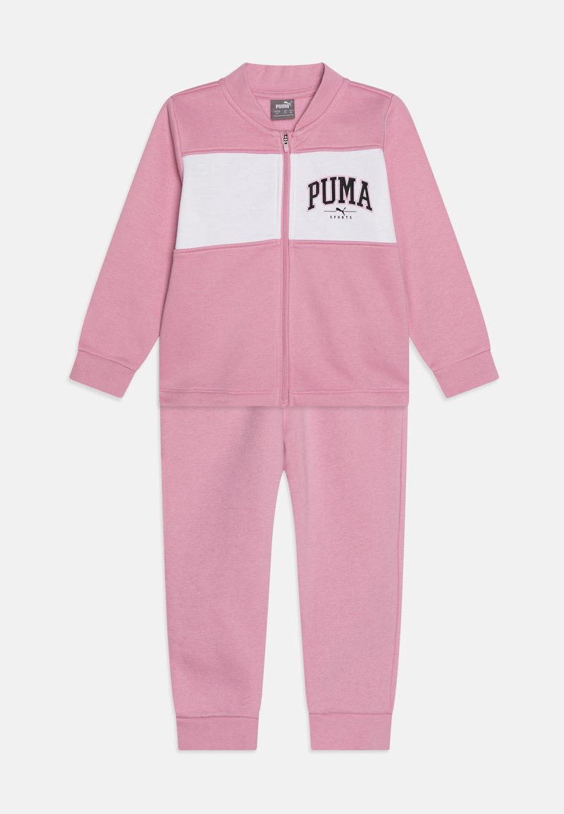 Survêtement rose en tissu doux, avec un panneau poitrine blanc et le logo "PUMA". Comprend une veste zippée et un pantalon assorti.