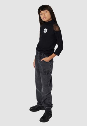 Maglione a collo alto nero a righe con dettagli trasparenti sulle spalle, abbinato a jeans larghi grigi scuri con stampa del logo nera. Stivali neri alla caviglia completano il look.