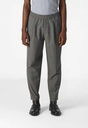 Osoba nosząca szare, dopasowane spodnie z elastycznym pasem oraz czarne skórzane botki, stojąca na białym tle.