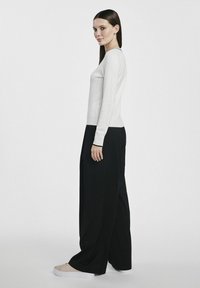 Biały, długi rękaw, zestawiony z luźnymi czarnymi spodniami. Materiał wydaje się miękki i gładki; buty w jasnym kolorze z sznurówkami.