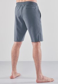 Harmaat puuvillashortsit rentomalla mitoituksella, vyötäröltä ja takataskusta, nähtynä takaviistosta. Sileä rakenne, polvenkorkuiset.