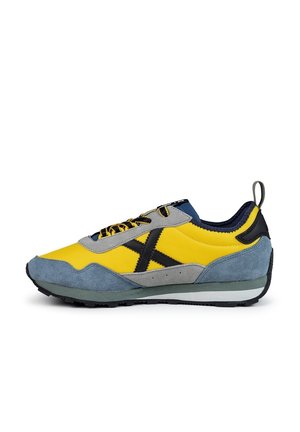 Baskets de sport jaunes et bleues avec un motif "X" noir, semelle grise, lacets noirs et jaunes, et languette au talon, vues de côté.