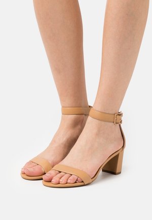 Sandales à talons carrés en cuir tan avec deux larges brides au niveau des orteils et une bride de cheville réglable dotée d'une boucle rectangulaire.