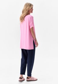 Różowa, oversize'owa koszulka z krótkimi, podwiniętymi rękawami, z bocznymi rozcięciami i prostym krojem. Połączona z luźnymi, granatowymi spodniami i różowymi trampkami.
