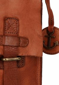 Borsa in pelle marrone con superficie texture, dotata di una tracolla ad anello e di un charm a forma di ancora attaccato da un anello in ottone.